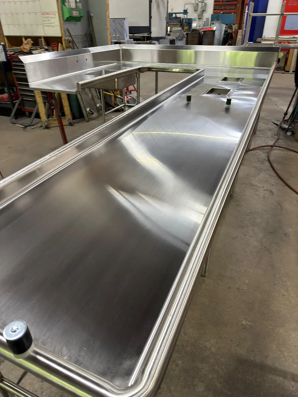 L shaped stainless prep counter with a raised rear edge, seen down its length in the shop