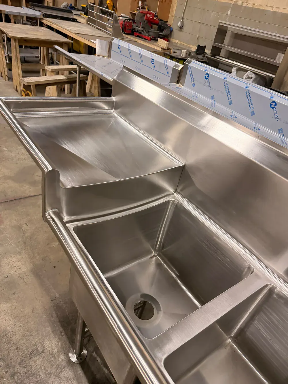 Stainless dish table with a scrap chute, sink bowl and sloped drainboard, standing on the shop floor