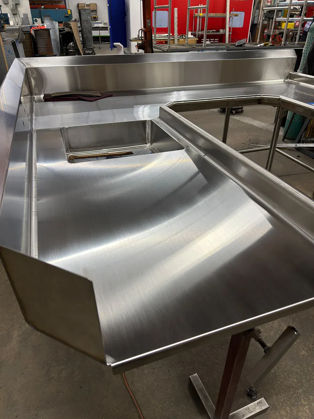 Close view of the wide flat deck of a corner dish table and the angled scrap chute panel welded into it