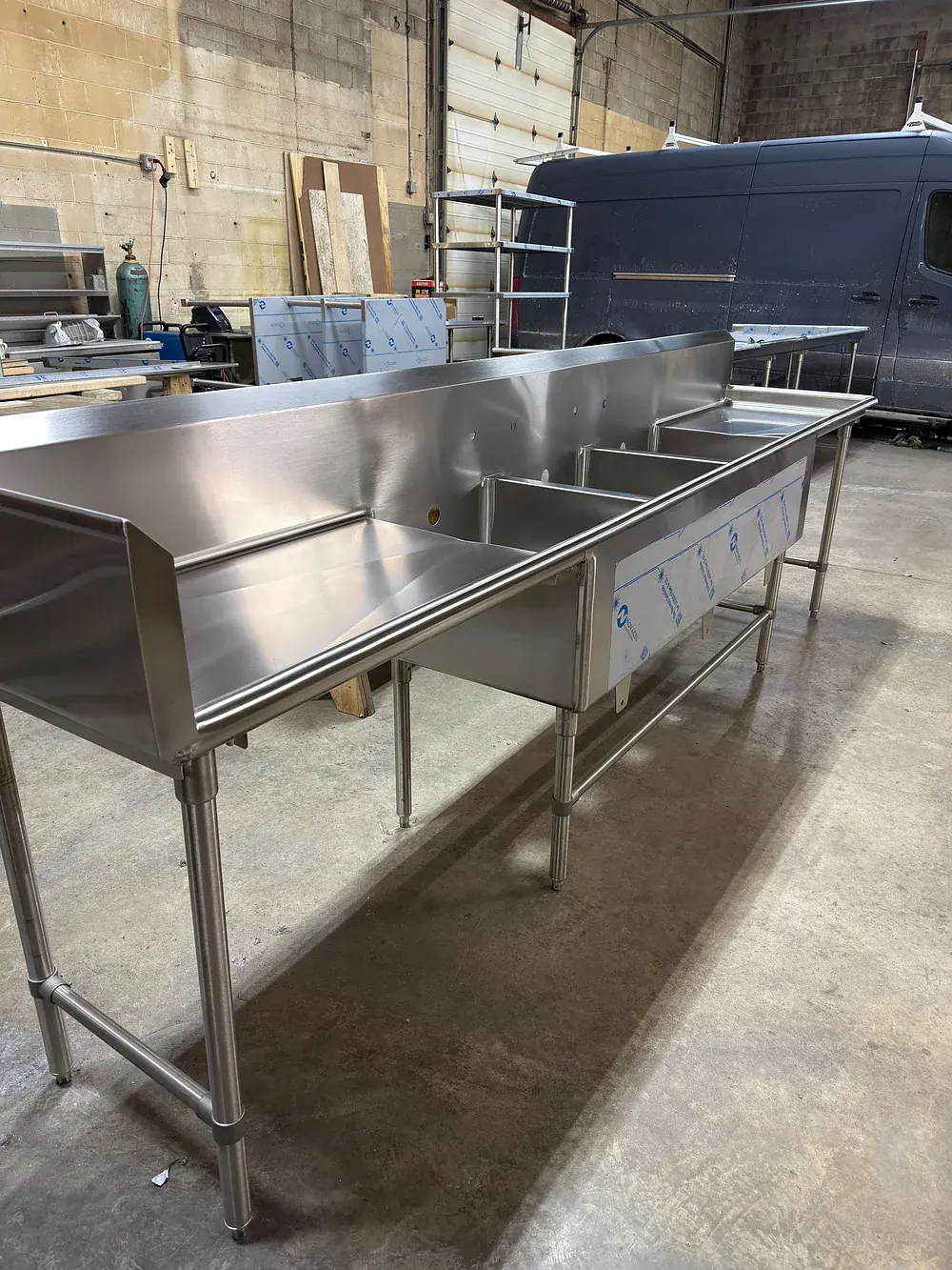 Three compartment stainless sink with drainboards on both ends, on adjustable legs
