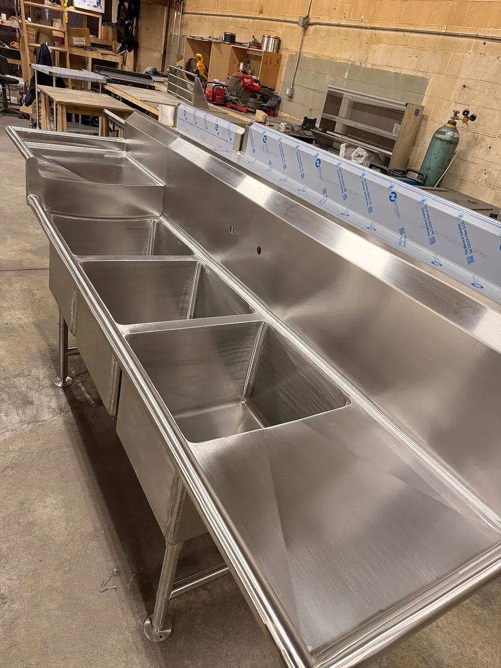 Long stainless sink run with three bowls and integral drainboards under shop lighting