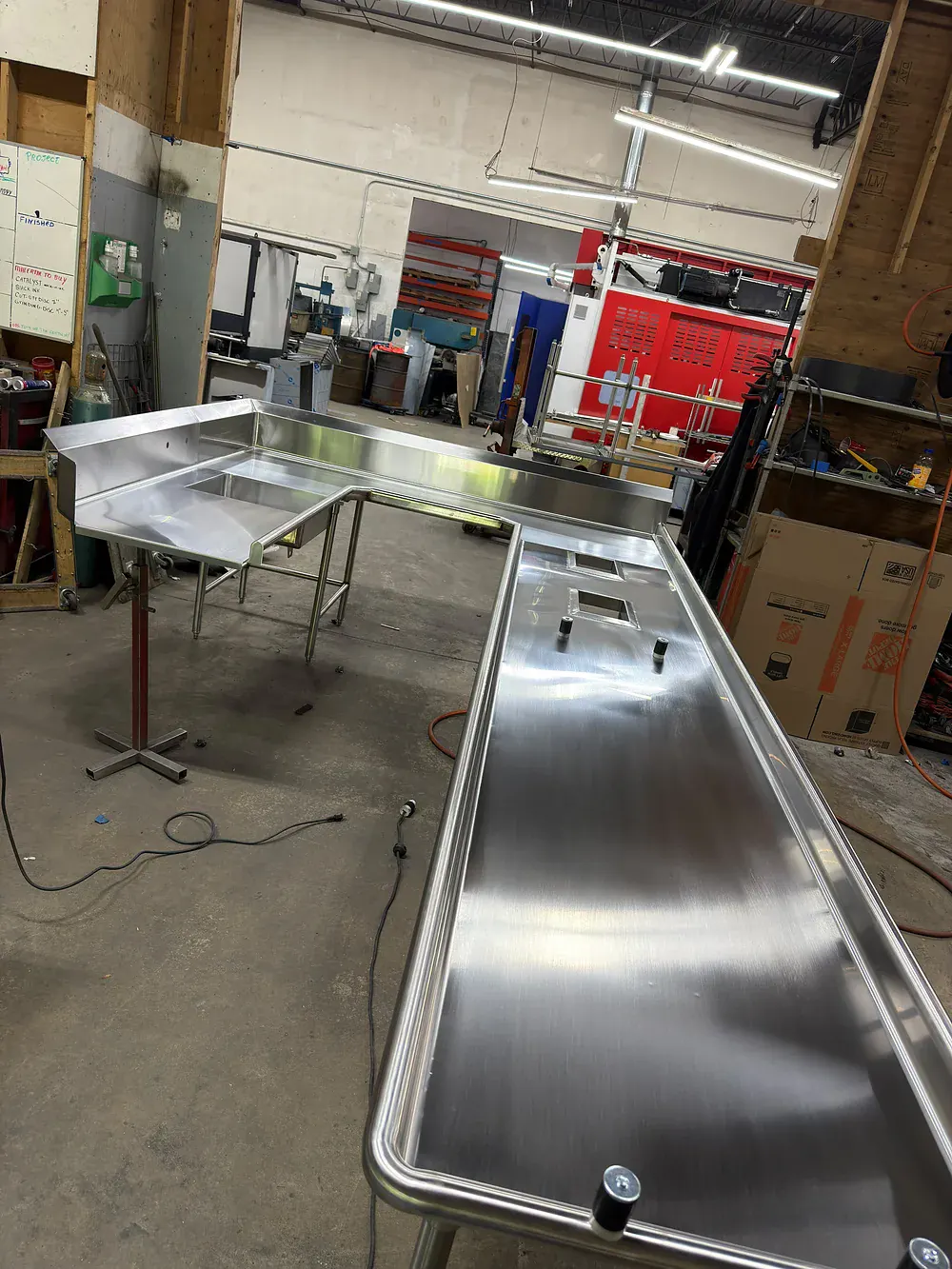 L shaped stainless counter with raised rear edge next to a dish table with drainboard on the shop floor