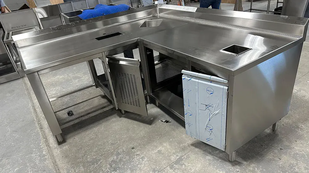 Stainless counter running over a refrigerated base with an open door, in the shop