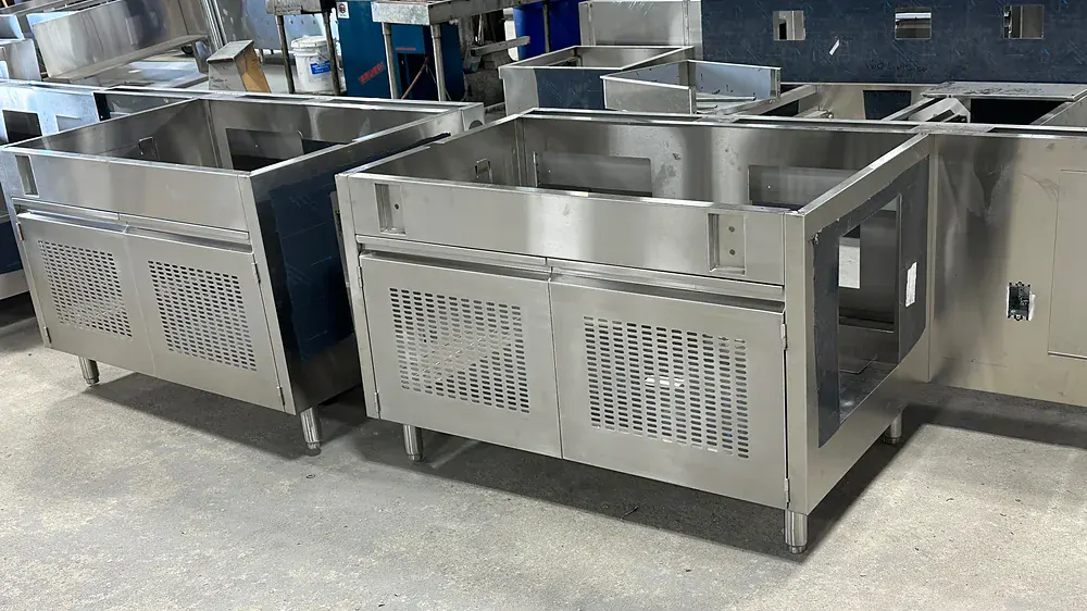 Row of stainless cooking stations with louvered ventilated bases, lined up on the shop floor