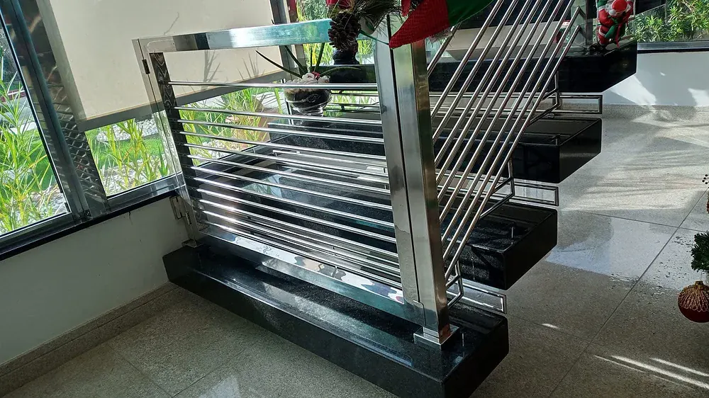 Stainless guardrail with closely spaced horizontal bar infill, set on a stone base at the foot of an open stair with stainless stringers and dark stone treads